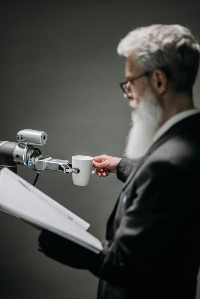 Elderly man interacts with robot arm holding a cup, showcasing innovation indoors.